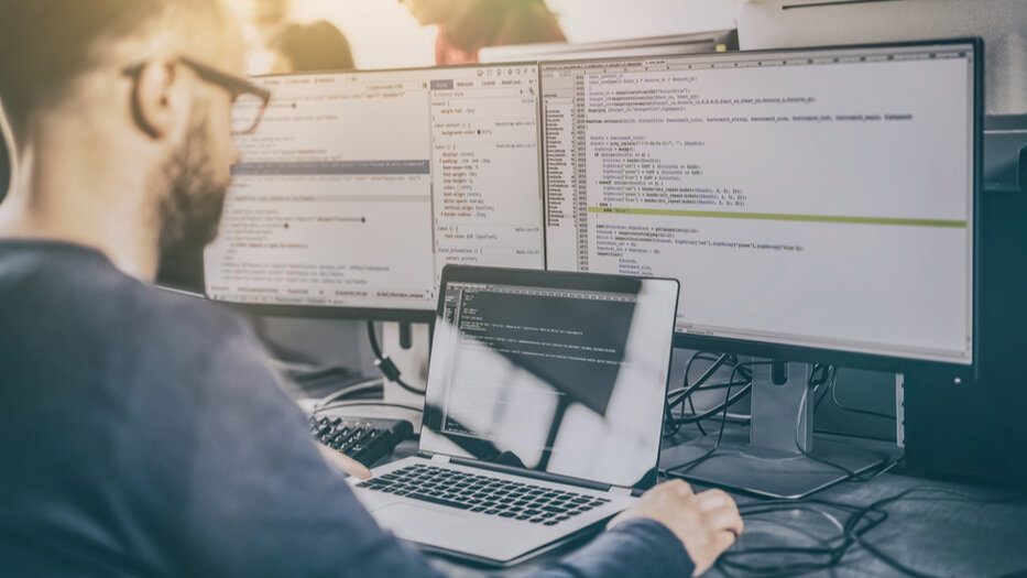 Man sits in front of screens showing source code